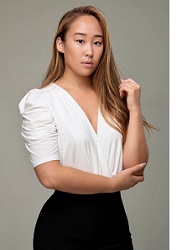 Rachel Maeng Brown in white blouse and black skirt against gray background